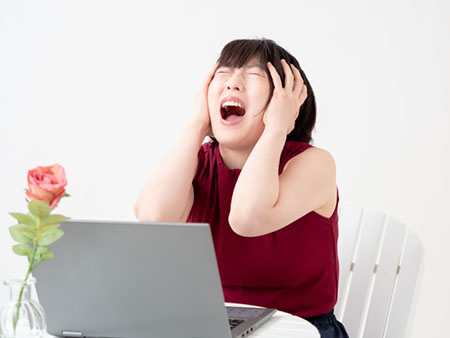 パソコン画面を前に頭を抱える女性