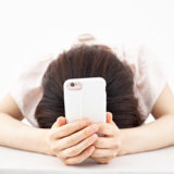 スマートフォンを手に顔を伏せる女性