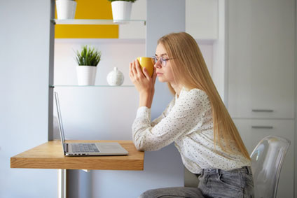 カップを手にPCを見つめる女性